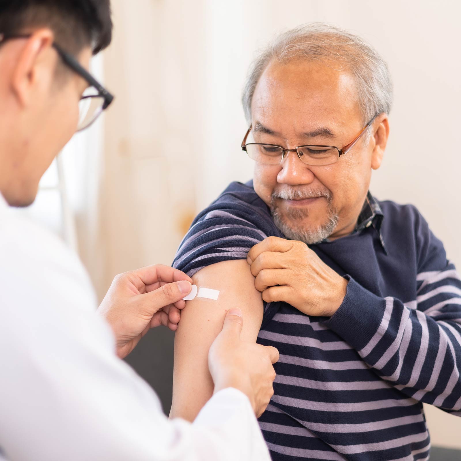 Doctor putting a bandaid on an older man’s arm.