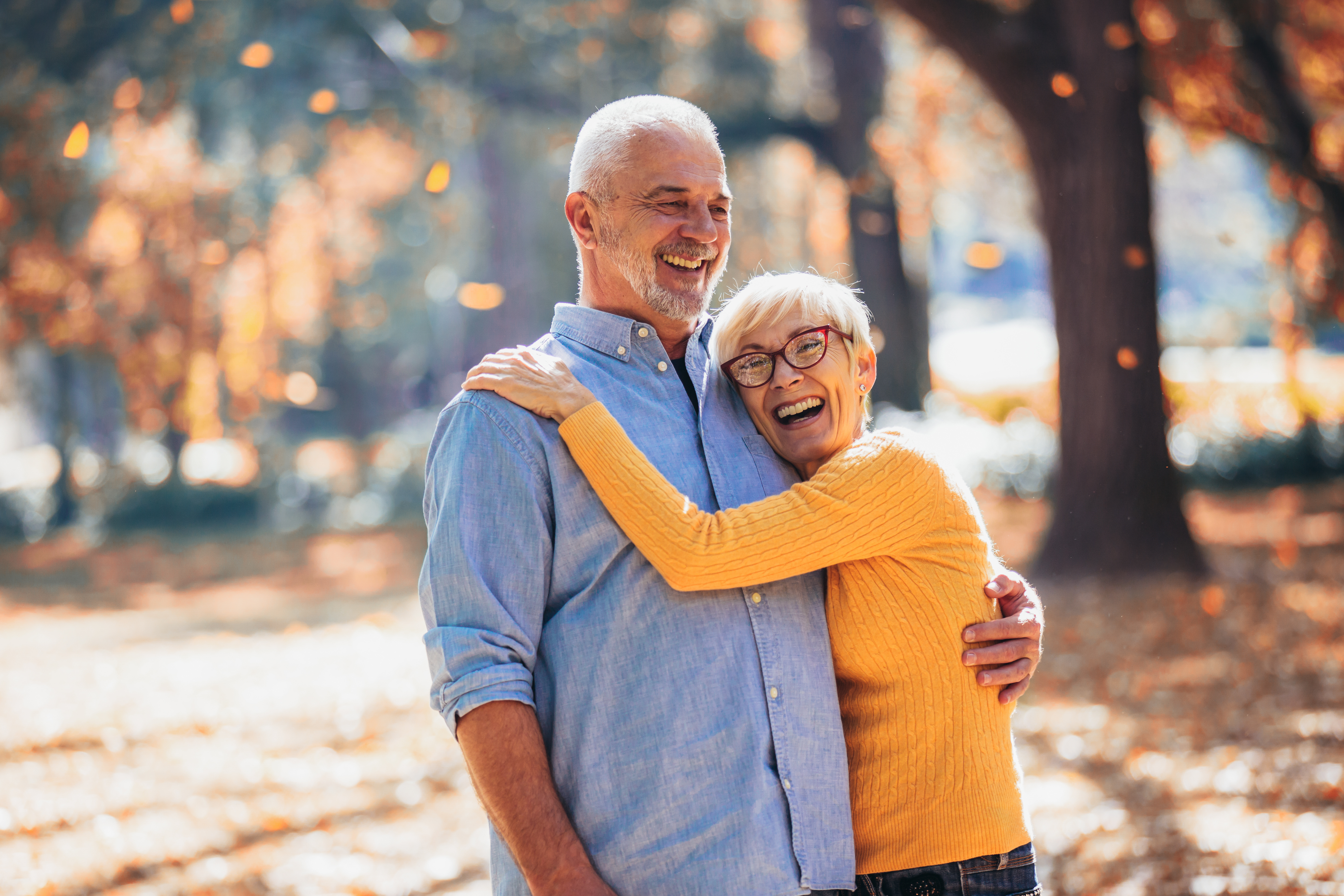 An older couple smiling and hugging outside.