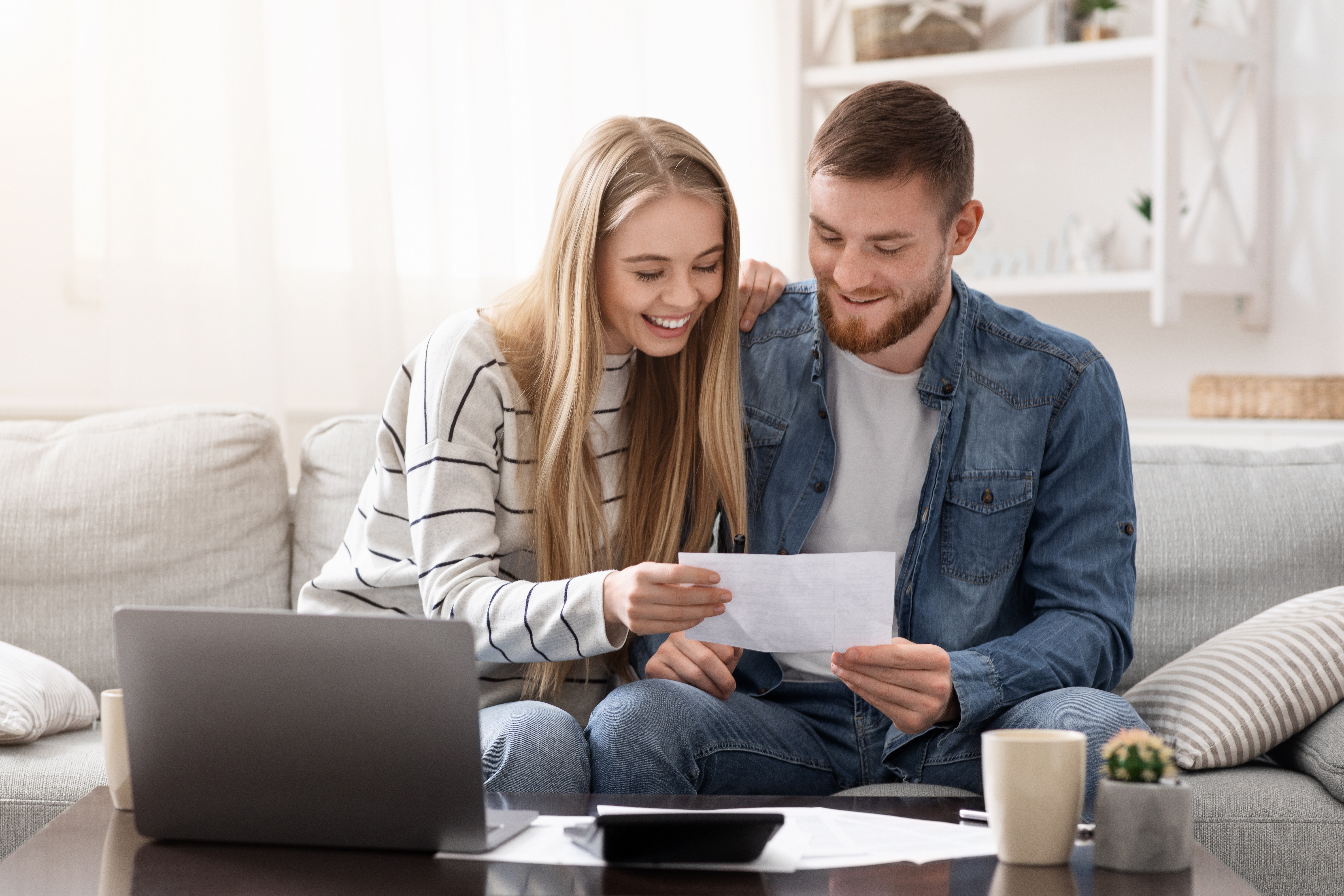 Young couple sitting on the couch looking at a document and smiling.
