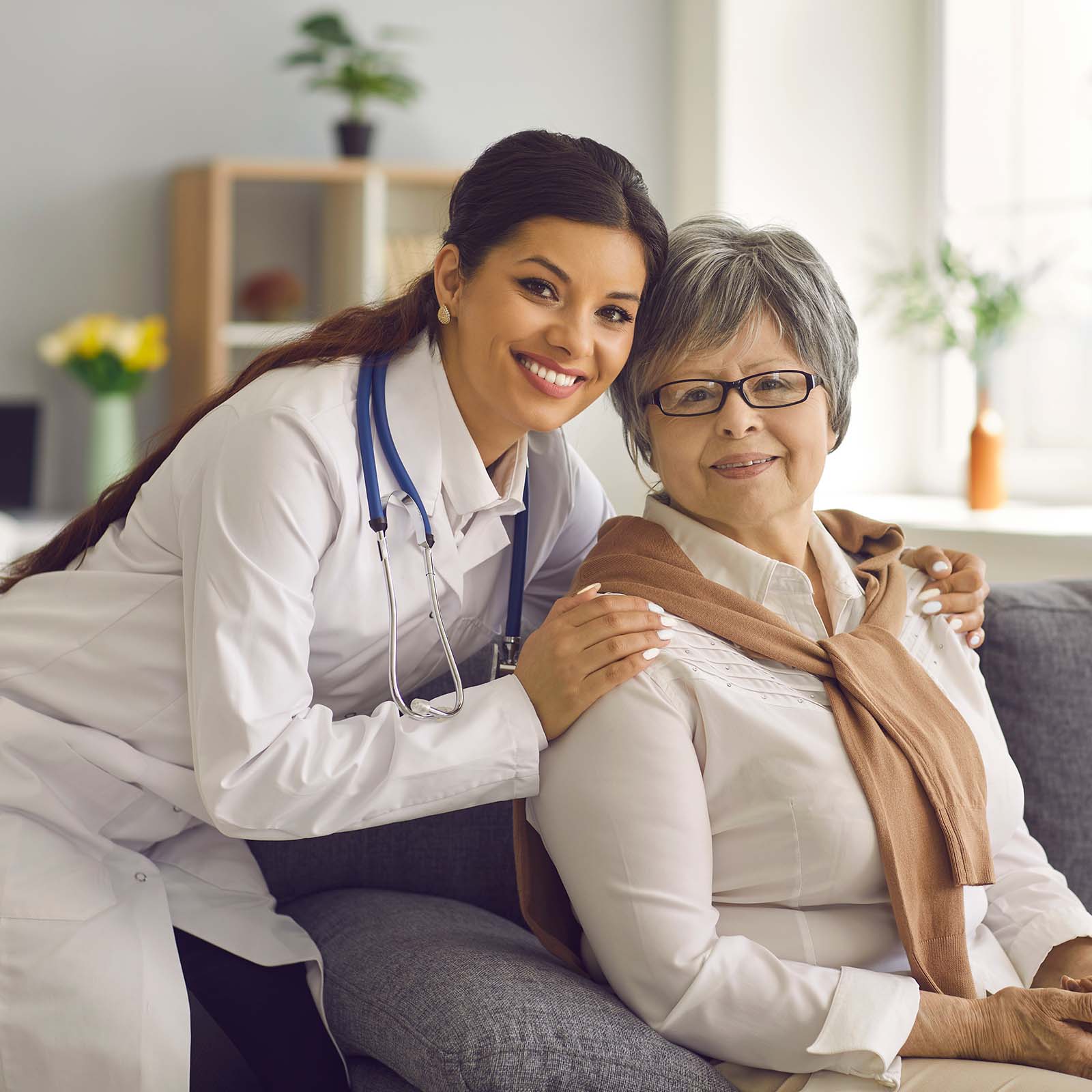 A physician posing next to older patient who is sitting on the couch